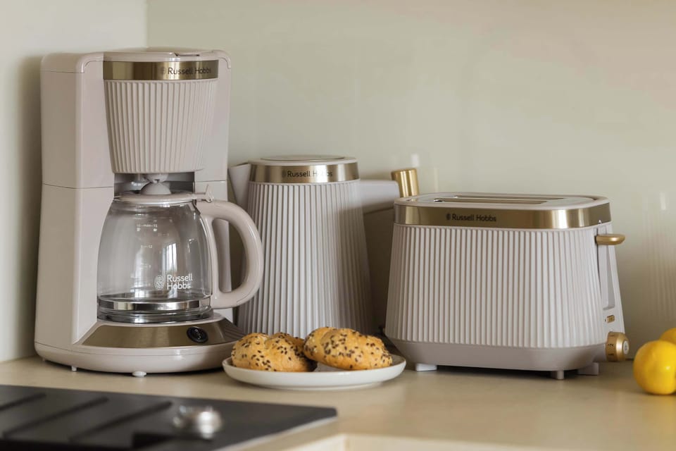 A kitchenette countertop with small appliances including a coffee maker and a toaster, placed next to a few pastries and a lemon. The setup is neat and practical, ideal for preparing breakfast.