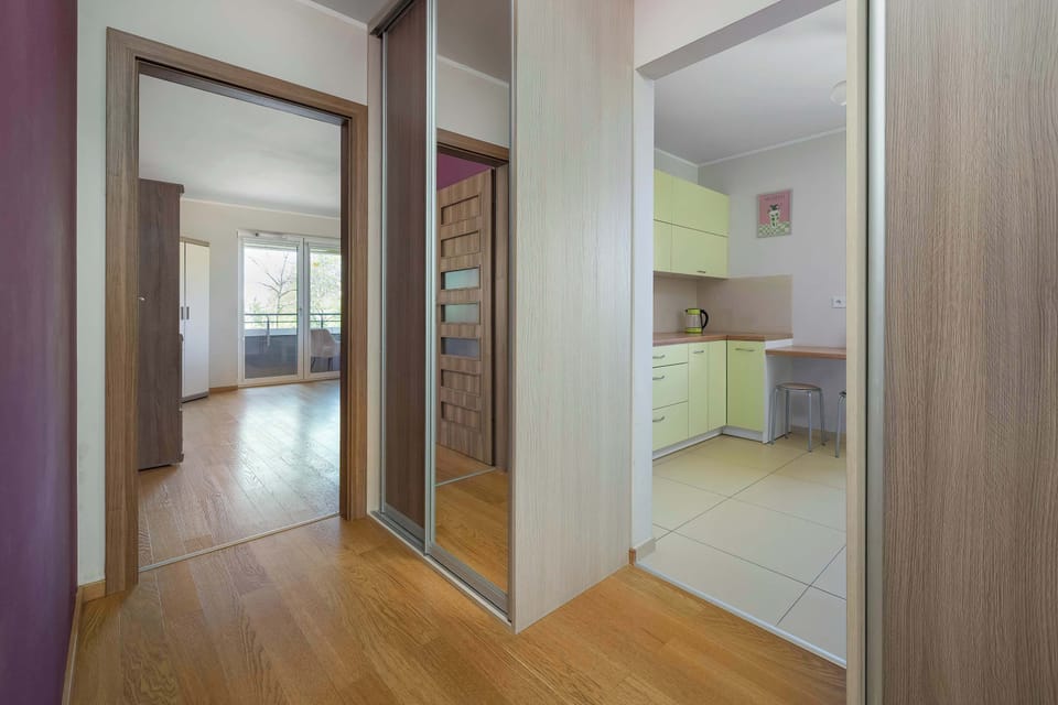 A functional hallway with mirrored wardrobe doors that visually enlarge the space and provide practical storage. From here, there is a clear view into the bright kitchen and the open living room, creating a sense of continuity and spaciousness.