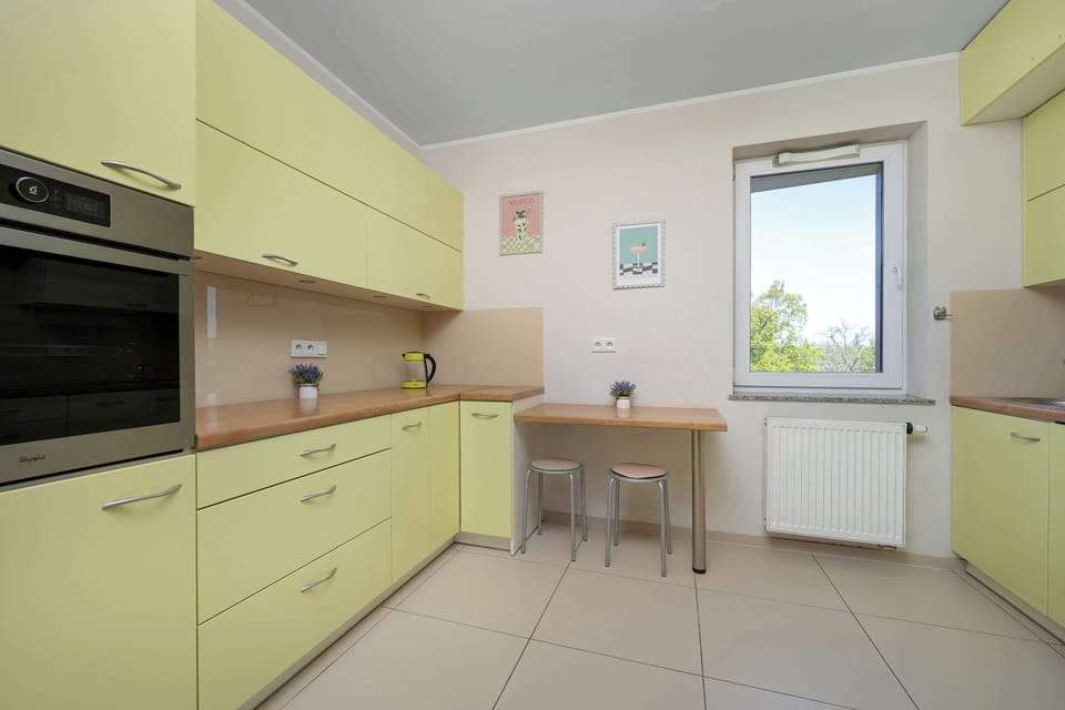 A bright kitchen with light-colored cabinets and a functional layout that offers plenty of storage and workspace. A window above the counter brings in natural light, making the space feel fresh and inviting.