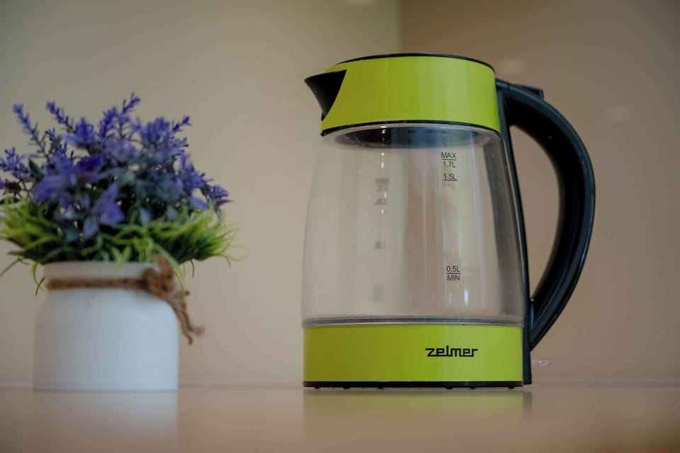 A close-up of a modern electric kettle placed on a kitchen counter. The bright color adds a lively accent to the space.