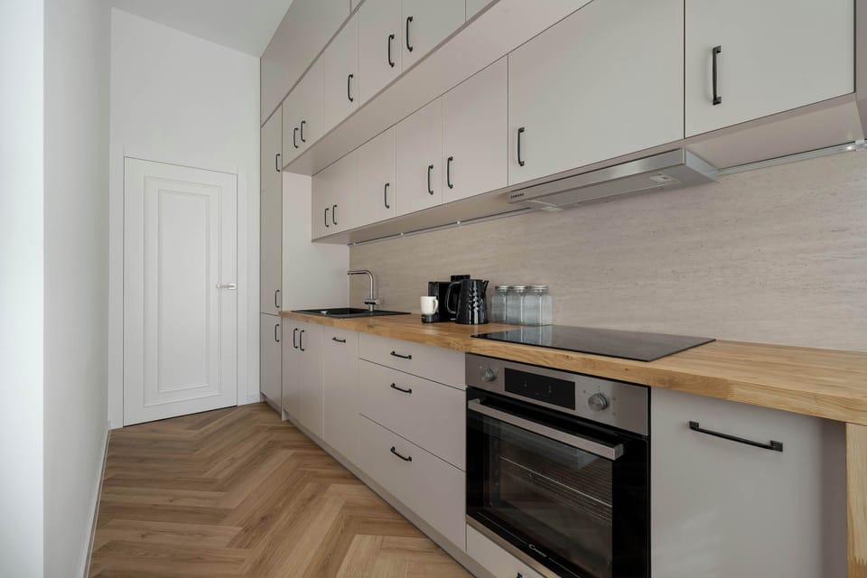 Another view of the kitchenette featuring cabinetry, a stovetop, and a built-in oven. The combination of white fronts and wooden elements creates a balanced, contemporary look. The layout supports comfortable cooking in a compact space.