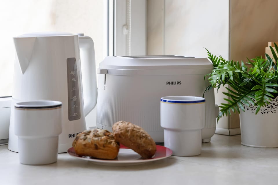 A close-up of a kitchen counter with a kettle, cups, and a plant. The setup feels cozy and ready for use.