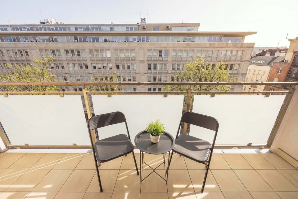 A balcony with a small table and two chairs, perfect for relaxing outdoors. The view overlooks nearby buildings.