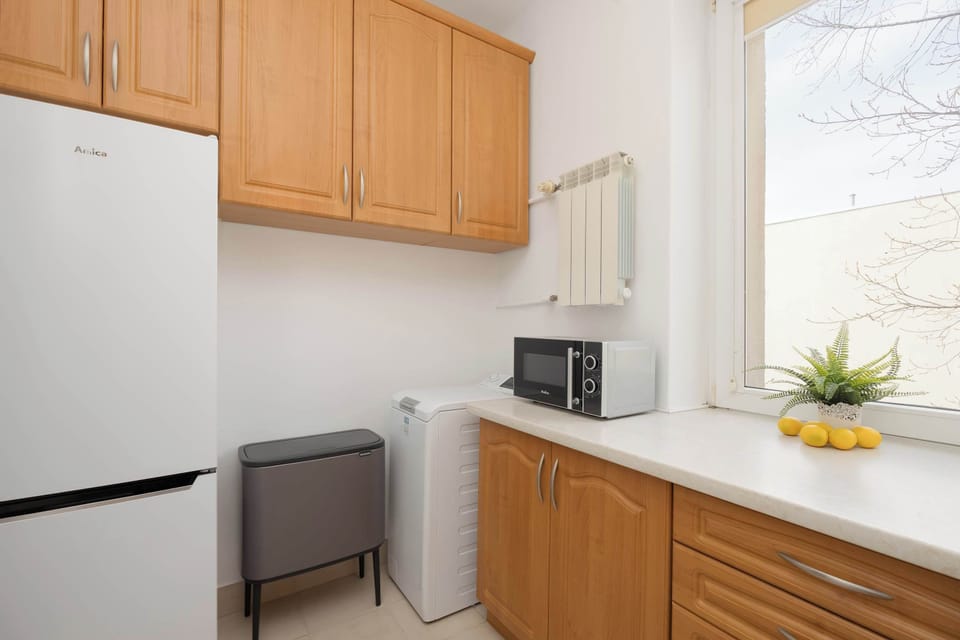 A bright kitchen with upper wooden cabinets and a small dining table. Natural light enhances the clean look.