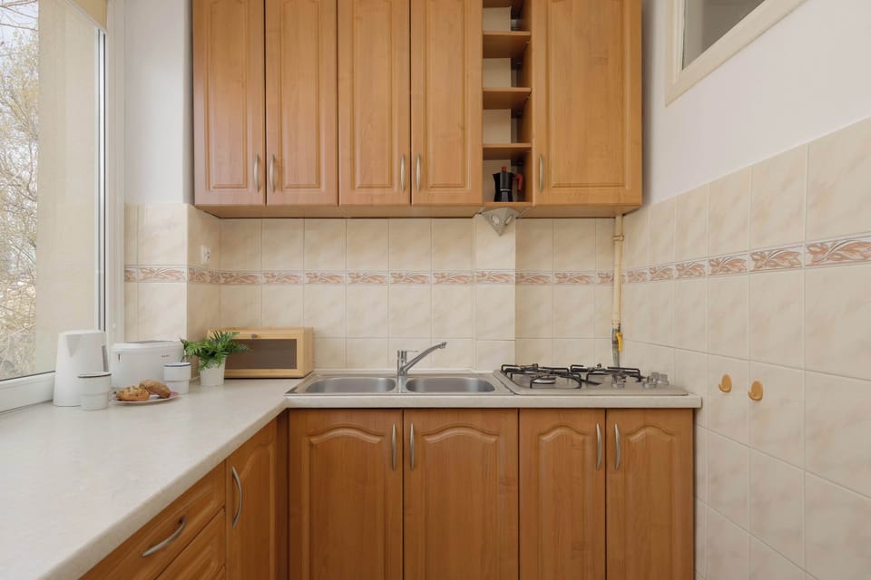 A kitchen with wooden cabinets, a light countertop, and tiled backsplash. The space is compact and functional.