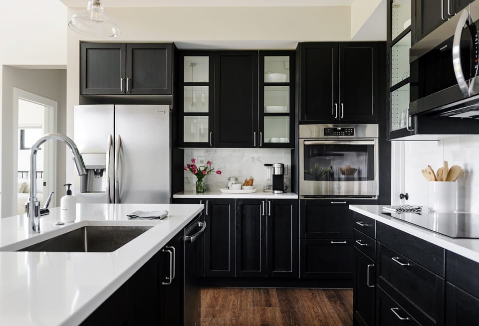 Dramatic black cabinetry pairs with stainless appliances and a marble subway-tile backsplash for a modern, timeless look.