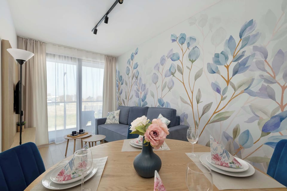 A dining table set with plates and decorative elements, positioned near a feature wall with a botanical mural. The space feels inviting and styled for a pleasant meal.