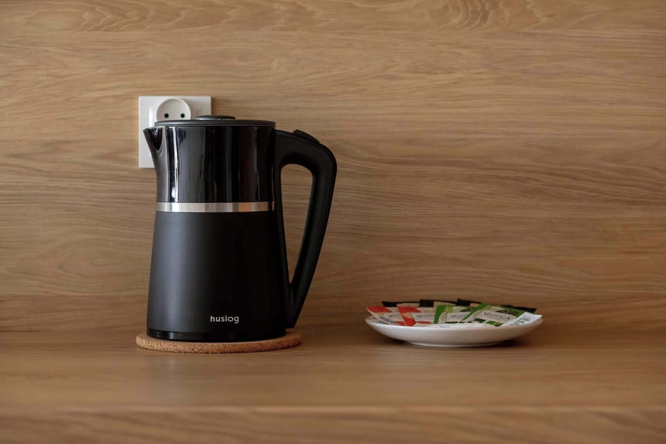 A close-up of a wooden countertop with a modern electric kettle and a small plate beside it. The setup suggests convenience for preparing hot drinks in a clean, minimalist space
