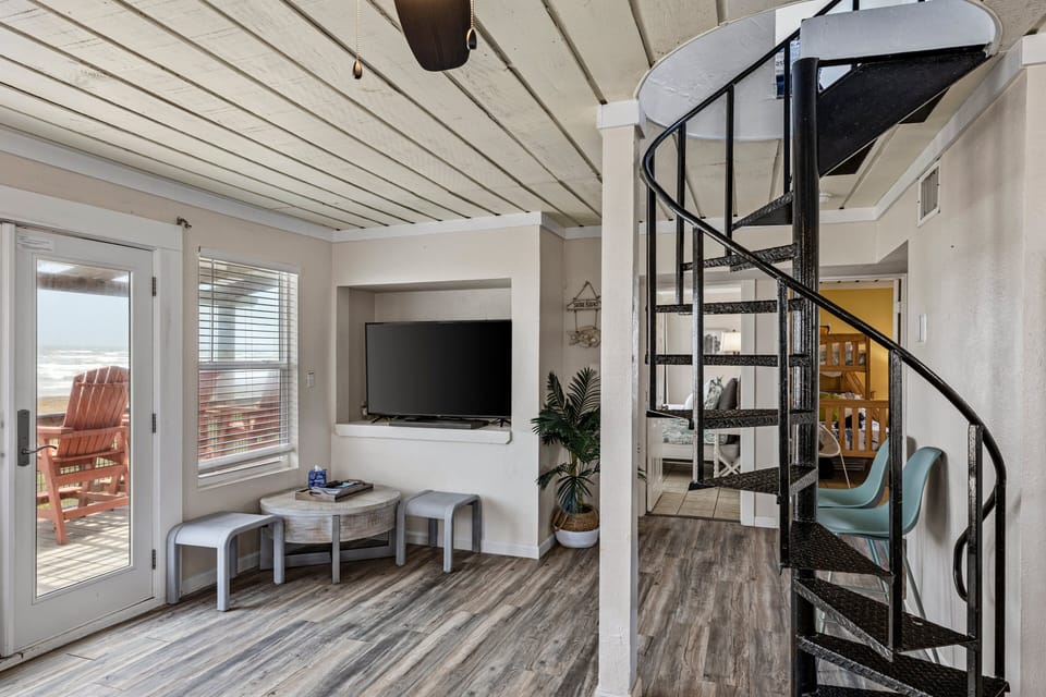 Modern living room with large flat-screen TV, spiral staircase, and open entertainment space designed for memorable group stays.