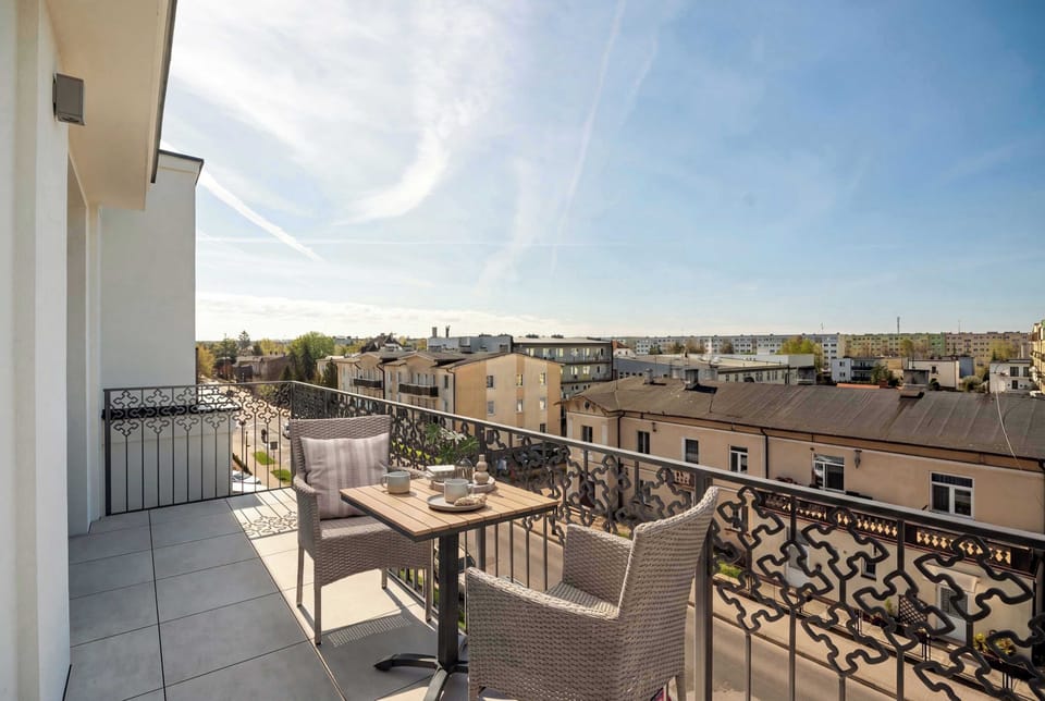A sunny balcony offers a quiet retreat with a small coffee table, comfortable wicker chairs, and a view over the city rooftops.