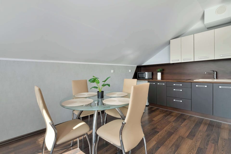 A dining area with a round glass table and several chairs. It sits next to a small kitchen, creating a practical eating space.