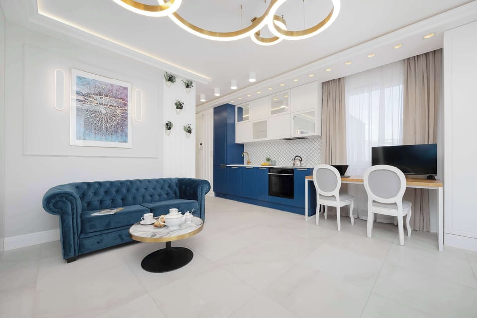 Looking across the main room, the deep blue sofa serves as a bold focal point against the white walls and light floors. A desk area is visible in the background, showing how the space transitions from relaxation to productivity.