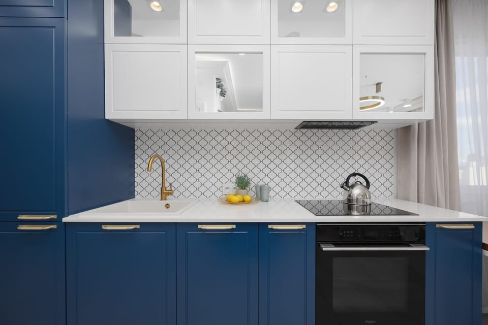 The kitchen area displays a striking contrast between navy blue lower cabinetry and minimalist white upper units. A textured hexagonal backsplash adds visual interest behind a modern black stovetop and stainless steel faucet.