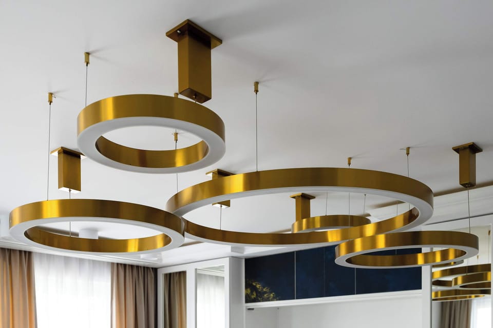 A close-up shot focuses on the intricate design of the gold circular lighting fixture mounted on the ceiling. The metallic finish adds a warm, glamorous element to the modern ceiling architecture.