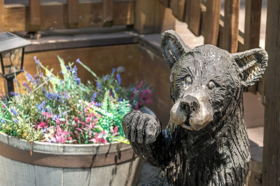 A charming bear sculpture greets visitors beside vibrant flower displays, creating a welcoming entrance to this mountain retreat.