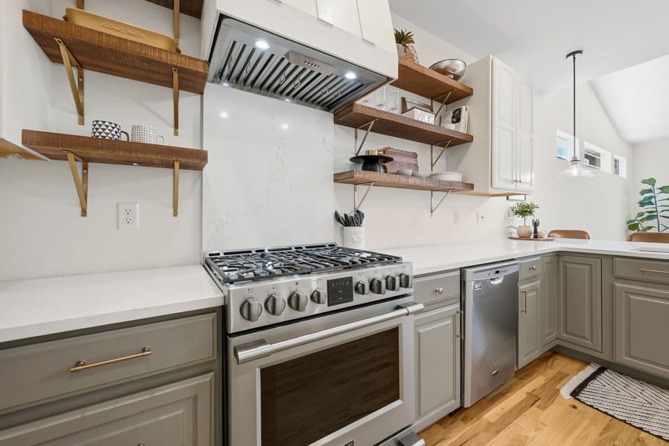 Modern kitchen, featuring a sleek gas range, open shelving, and stainless appliances.