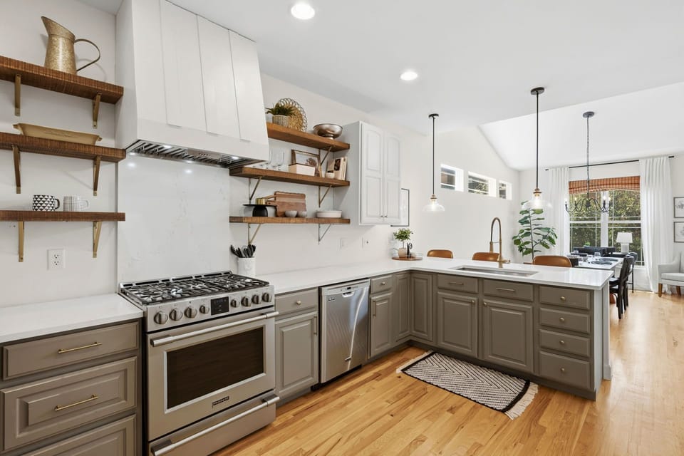 Fully equipped kitchen with open wood shelving, stainless steel appliances, and warm natural light.