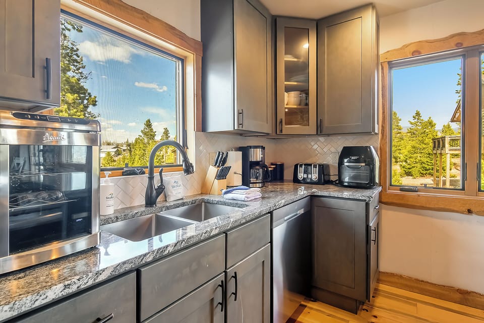 Your fully equipped kitchen features granite counters and forest views through large windows, perfect for morning coffee rituals.
