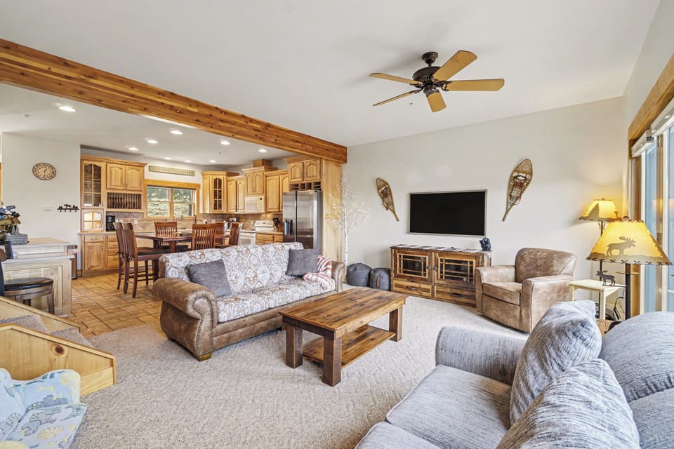 Relax in your spacious living room featuring rustic wood beams, cozy seating, and an open kitchen perfect for gathering.