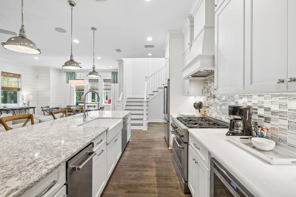 Gather around this stunning gourmet kitchen with gleaming granite counters, modern appliances, and a spacious island—your culinary headquarters with a view into the bright living area and staircase beyond.