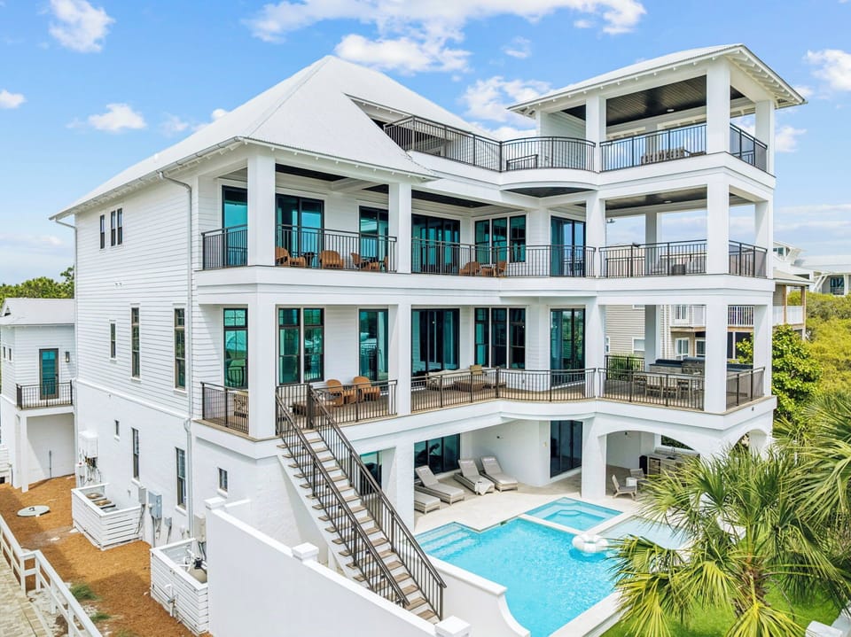 Elegant white multi-story vacation home featuring multiple private balconies, stunning pool area, and tropical landscaping in a peaceful residential setting.