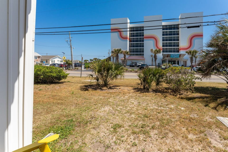 View across the street showcases the colorful beachside neighborhood with tropical palm landscaping and local businesses nearby.
