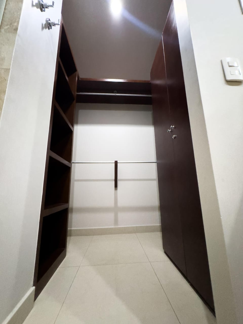 Walk-in closet featuring dark wood shelves, hanging rods, and light beige tiled flooring.