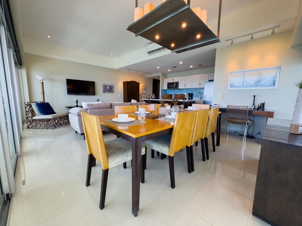 Dining area with a rectangular wood table and eight chairs set on glossy cream tile floors next to sliding glass doors.