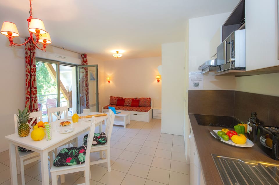 Dining table set for breakfast with the kitchen alongside — chandelier overhead, balcony just steps away