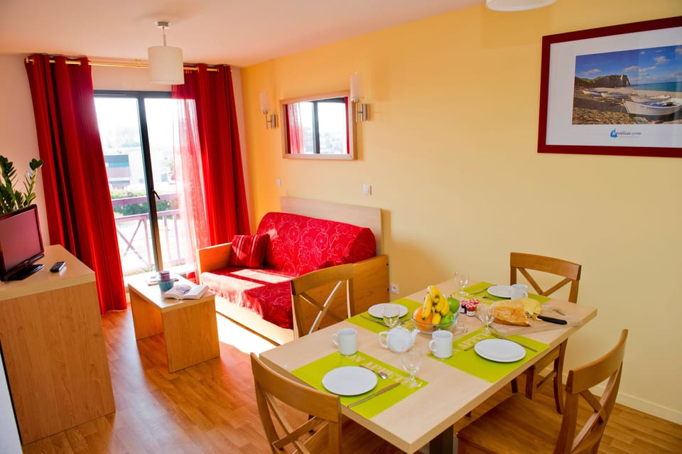 Living area with red sofa, dining table, and TV — the sofa converts to a bed for 2 additional guests