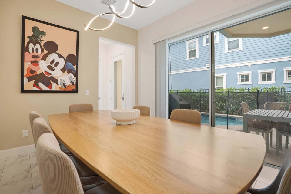 Dining area with a large wooden table and sliding glass doors opening to a poolside patio.