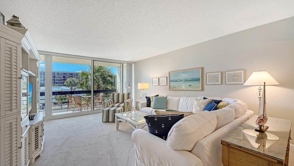 Living room with white sectional sofa, glass-top coffee table, striped armchair, and sliding glass doors to balcony.