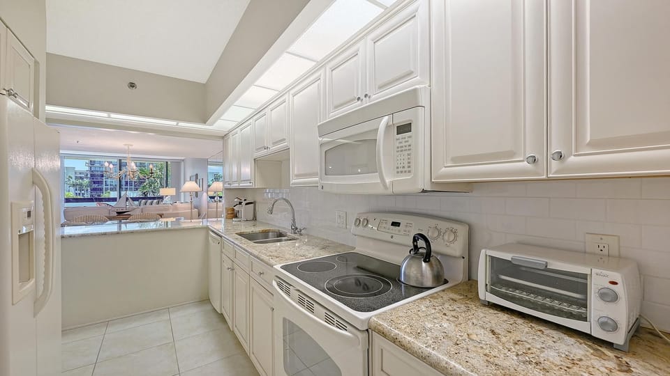 Galley kitchen with granite countertops, white cabinetry, electric stove, and toaster oven by pass-through window.
