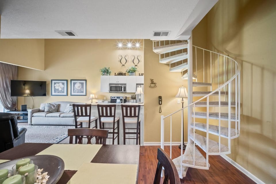 Spiral staircase with carpeted steps curves beside yellow walls and hardwood flooring near the dining table.