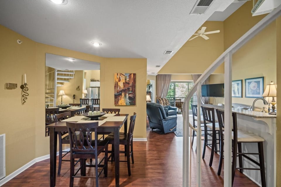 Dark wood dining table with six chairs sits beside a large wall mirror and warm yellow walls.