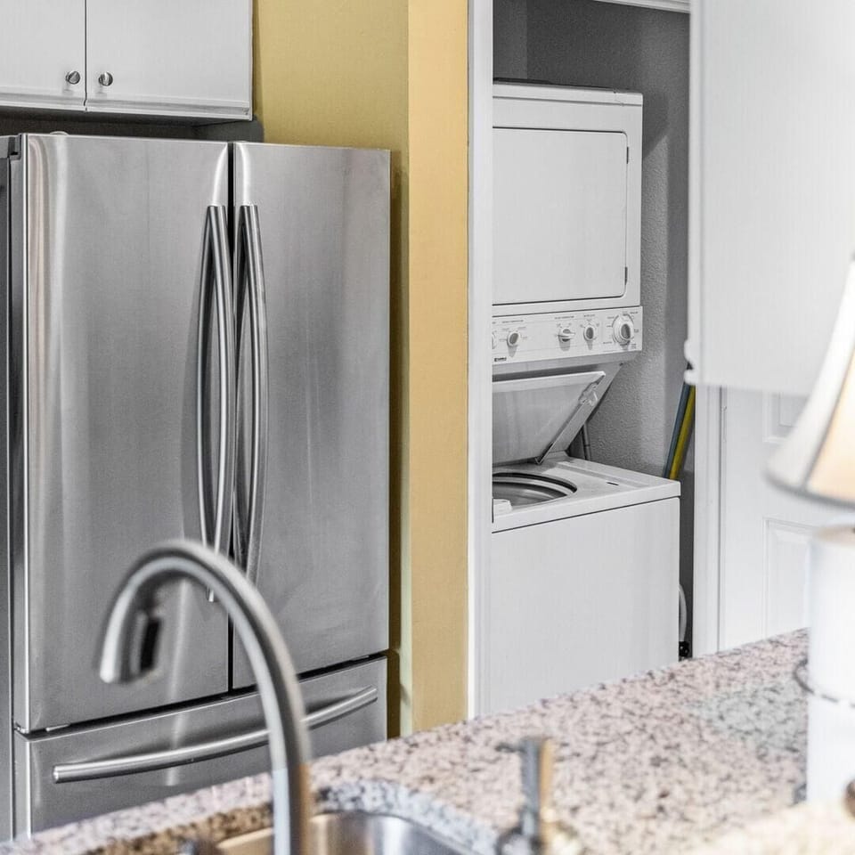 Kitchen nook with stainless steel refrigerator beside a white stacked washer and dryer unit.