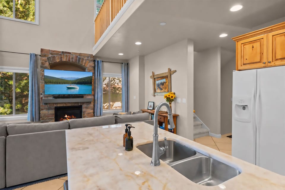 The spacious open living area seamlessly connects the kitchen and family room, featuring a cozy fireplace, 65 inch Smart TV with JBL soundbar, and comfortable gathering spaces perfect for relaxing after a day at the lake or slopes.