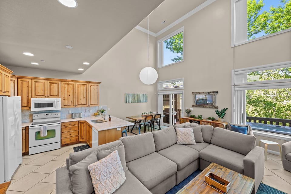 Bright and airy open-concept living space featuring vaulted ceilings, a fully equipped kitchen, cozy sectional seating, and large windows showcasing beautiful Pineview Reservoir views.