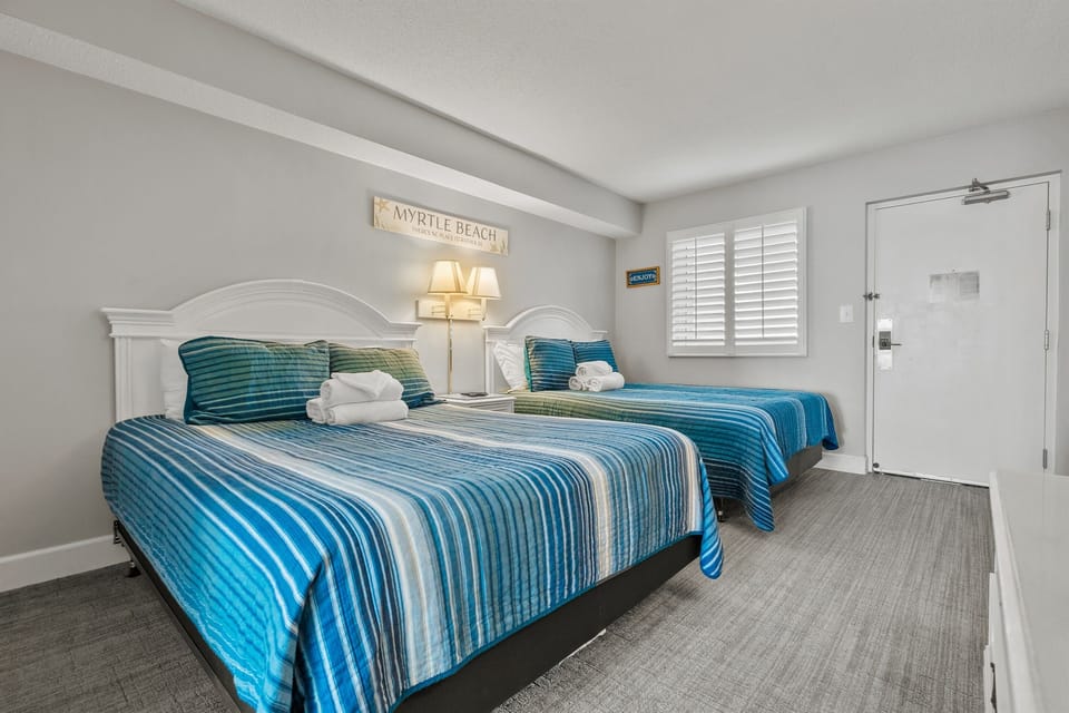 Bedroom with two queen beds, a smart tv, night stand, dresser, and a closet for personal effects.