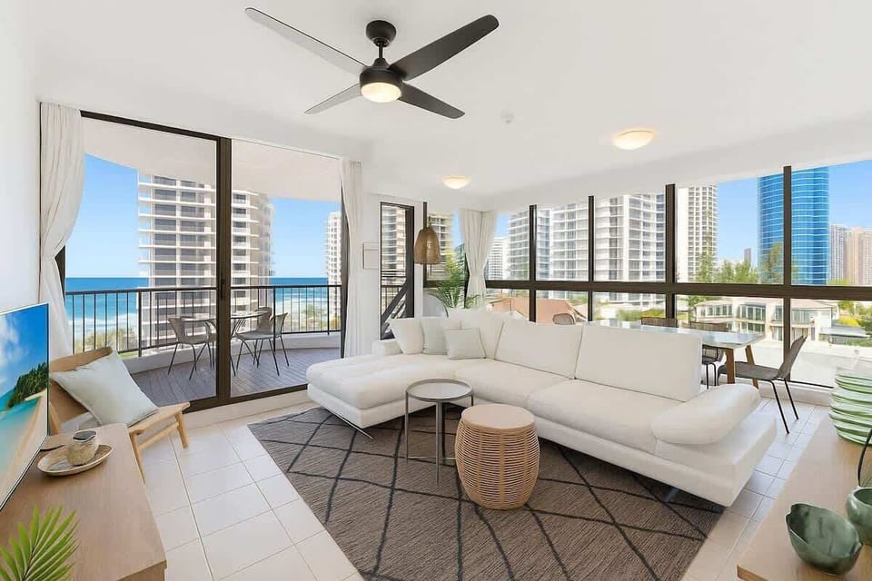 Bright open-plan living room with comfortable seating and ocean views and single sofa bed. Aircon only in bedroom. Fan on ceiling.