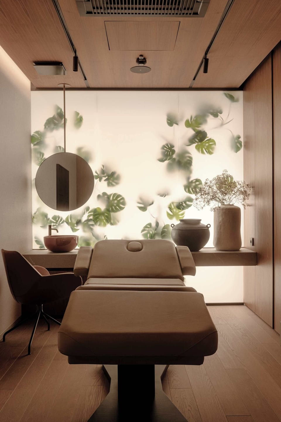 A serene spa or treatment room containing an adjustable massage table positioned in the center. The backdrop features soft interior lighting and a wall decorated with subtle botanical prints.