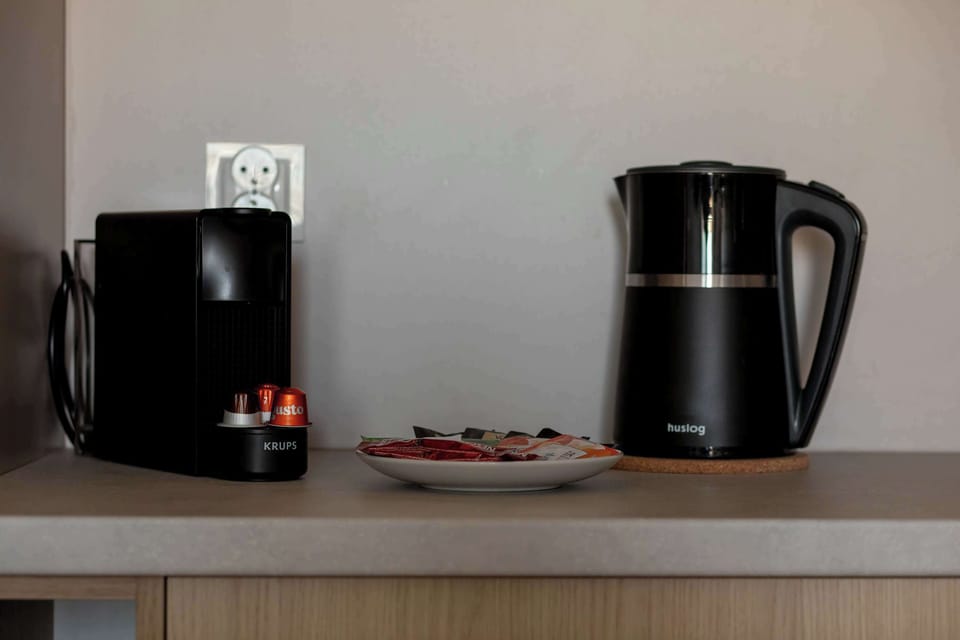 A close-up of a kitchenette countertop with a coffee machine and an electric kettle placed neatly side by side. A small tray with cups and accessories adds a practical and organized touch.