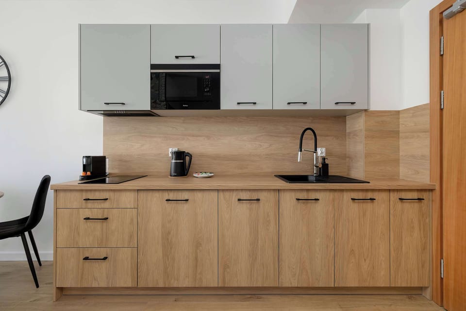 A closer view of the kitchenette, highlighting sleek cabinetry, a countertop, and built-in appliances. The design is minimalistic, with a tidy layout and warm wood finishes contrasting with white walls.