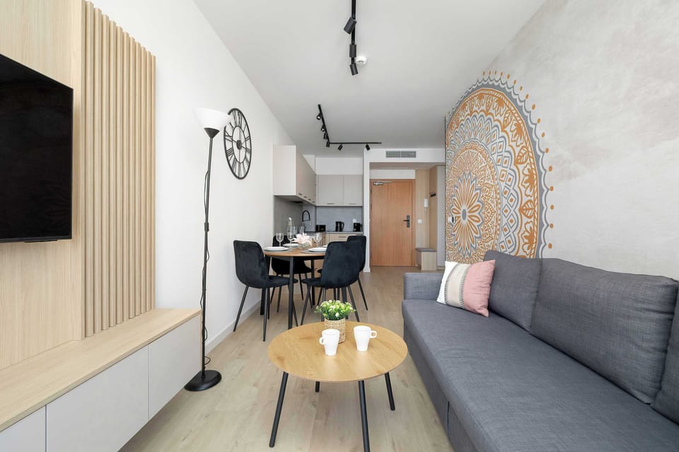 The living space is shown looking toward the kitchenette and entrance, highlighting the spacious flow. Light wood-effect flooring and track lighting tie the different functional zones together.