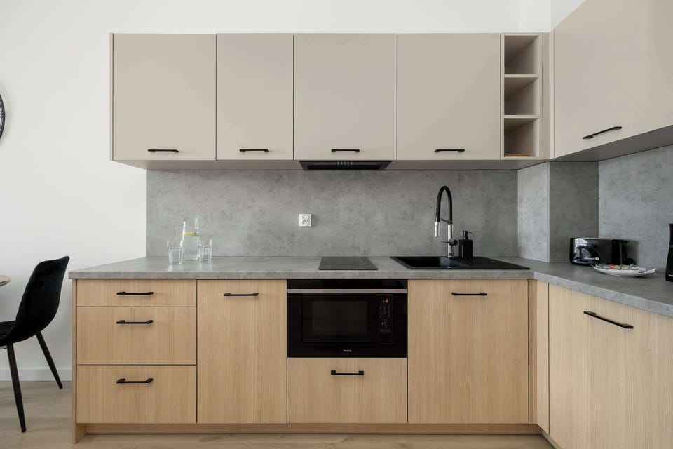 This linear kitchenette is designed with light-wood lower cabinets and beige upper units. It includes integrated appliances and a grey stone-effect backsplash for a clean, modern look.