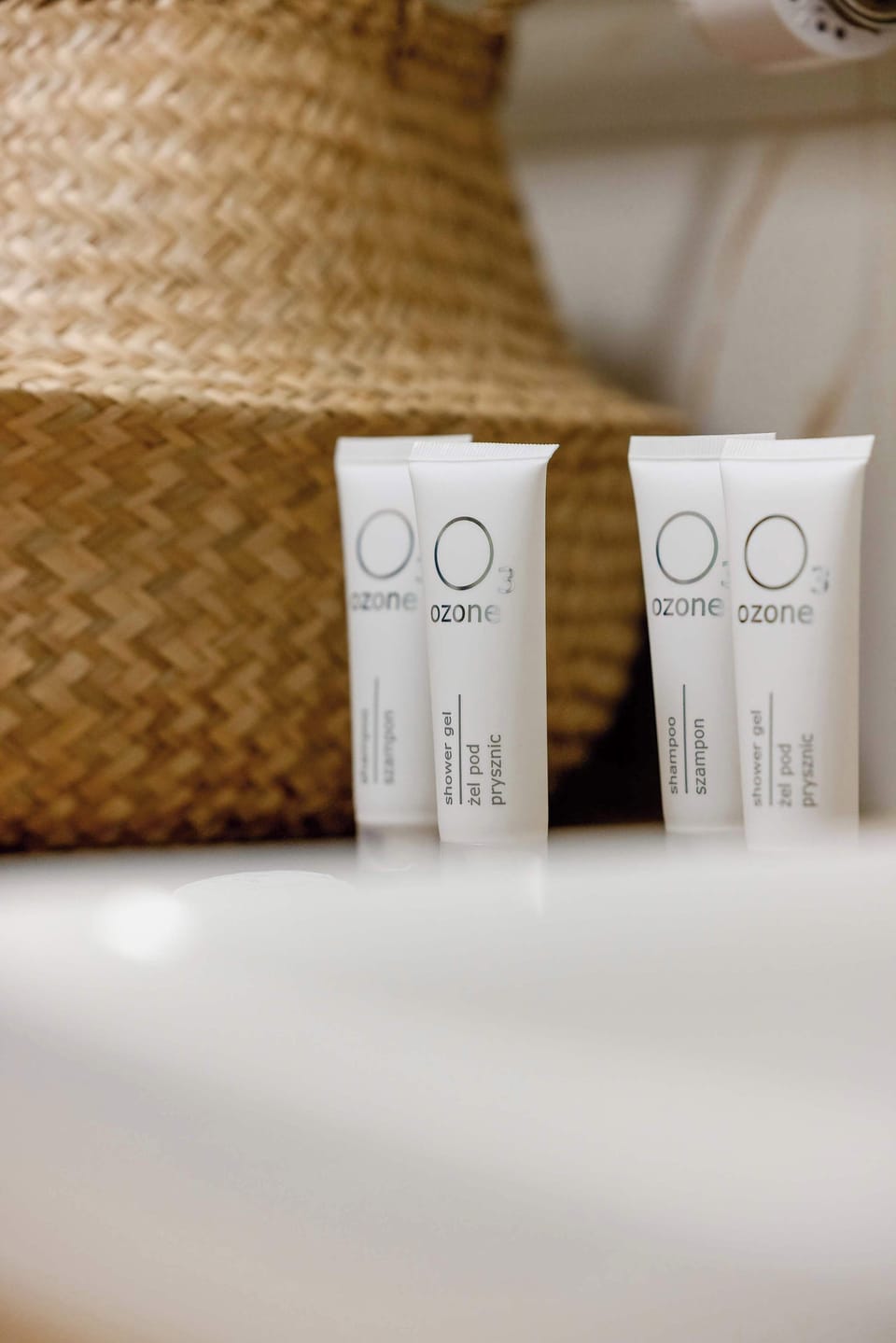 A detail shot focuses on complimentary toiletries placed on the edge of the white ceramic sink. A wicker basket in the background adds a natural, spa-like touch.