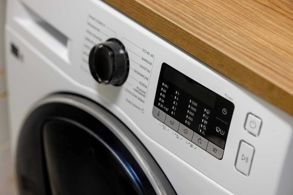 A close-up of the washing machine control panel shows various settings for laundry care. The machine is tucked under a sturdy wooden countertop.
