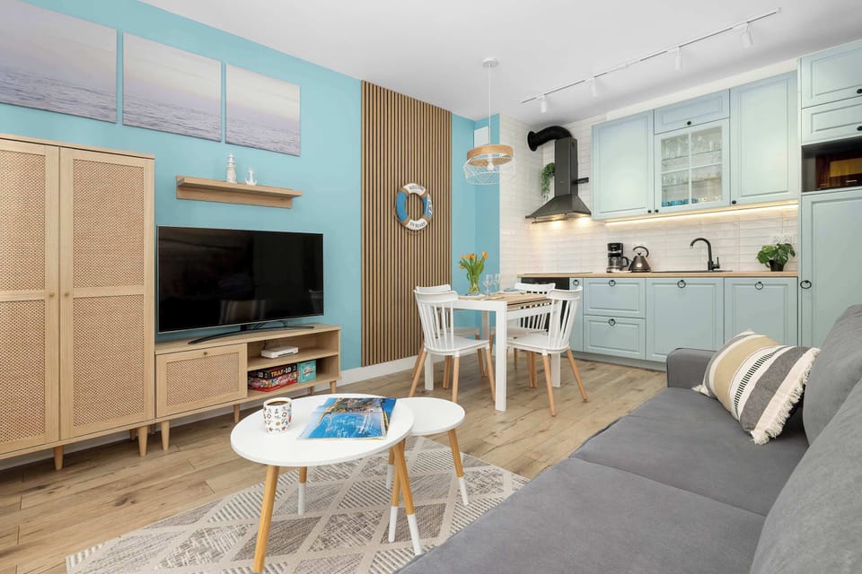 This wide shot of the open-plan living space connects the kitchenette, dining area, and lounge. The consistent use of light wood and blue tones creates a harmonious and airy feel.