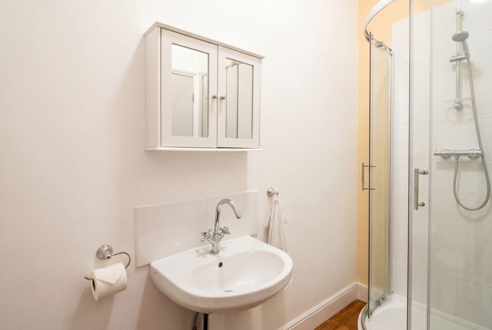 Clean en-suite shower room with chrome fittings, mirrored cabinet, and a glass-enclosed power shower.