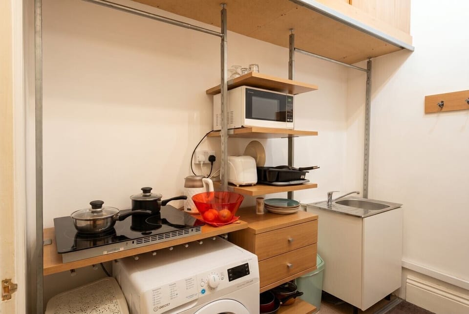 Compact kitchen stocked with a hob, microwave, toaster, cookware, and an in-unit washing machine.